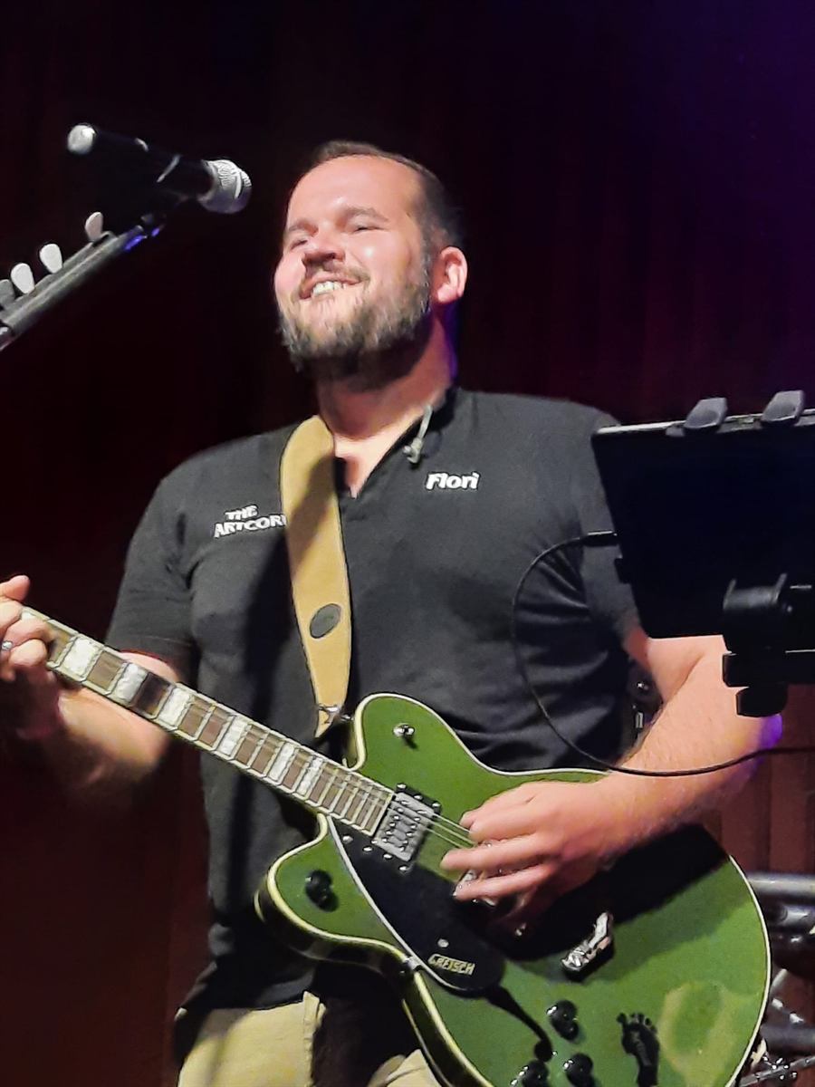 Gitarrist mit grüner Gitarre lacht am Mikrofon