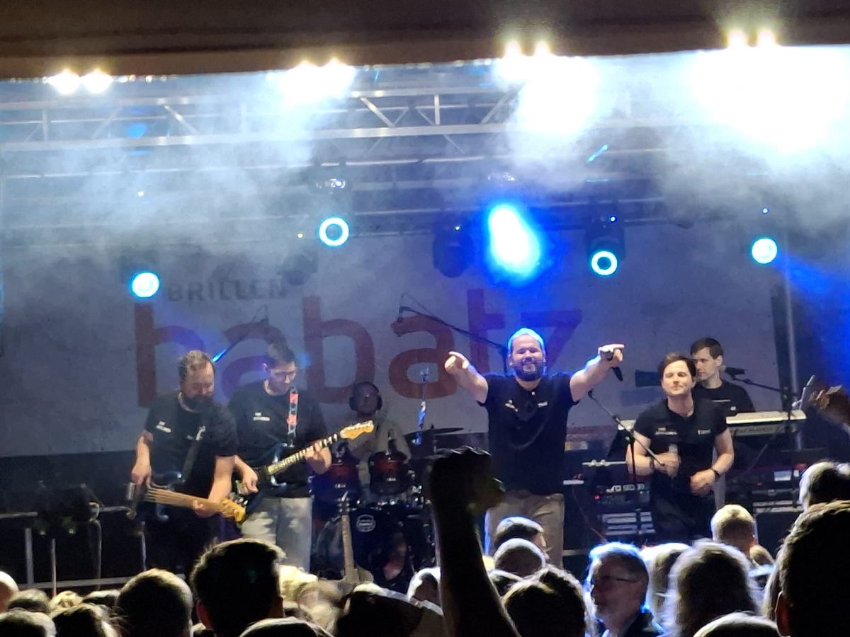 Band auf einer Open-Air-Bühne in blauem Licht, Sänger zeigt ins Publikum